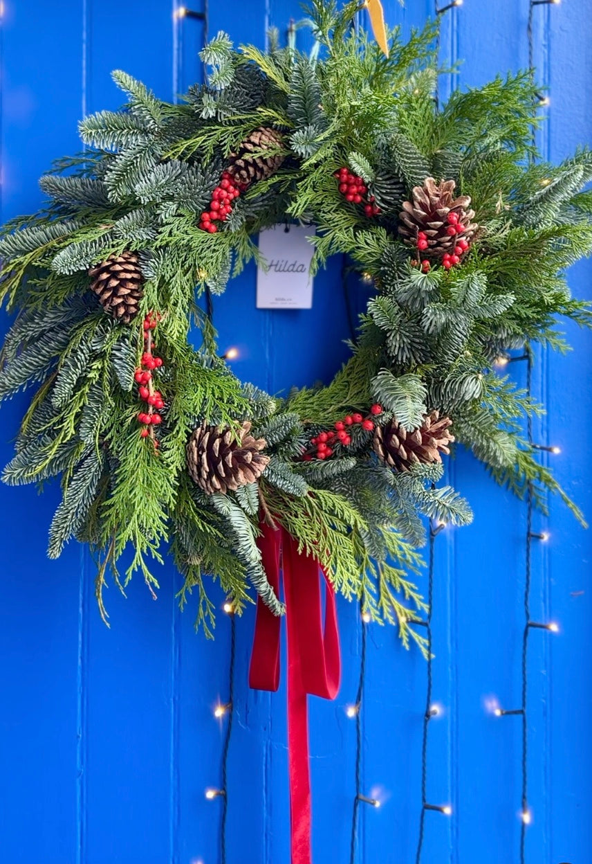 Christmas wreath with pine cones and red berries on a blue background