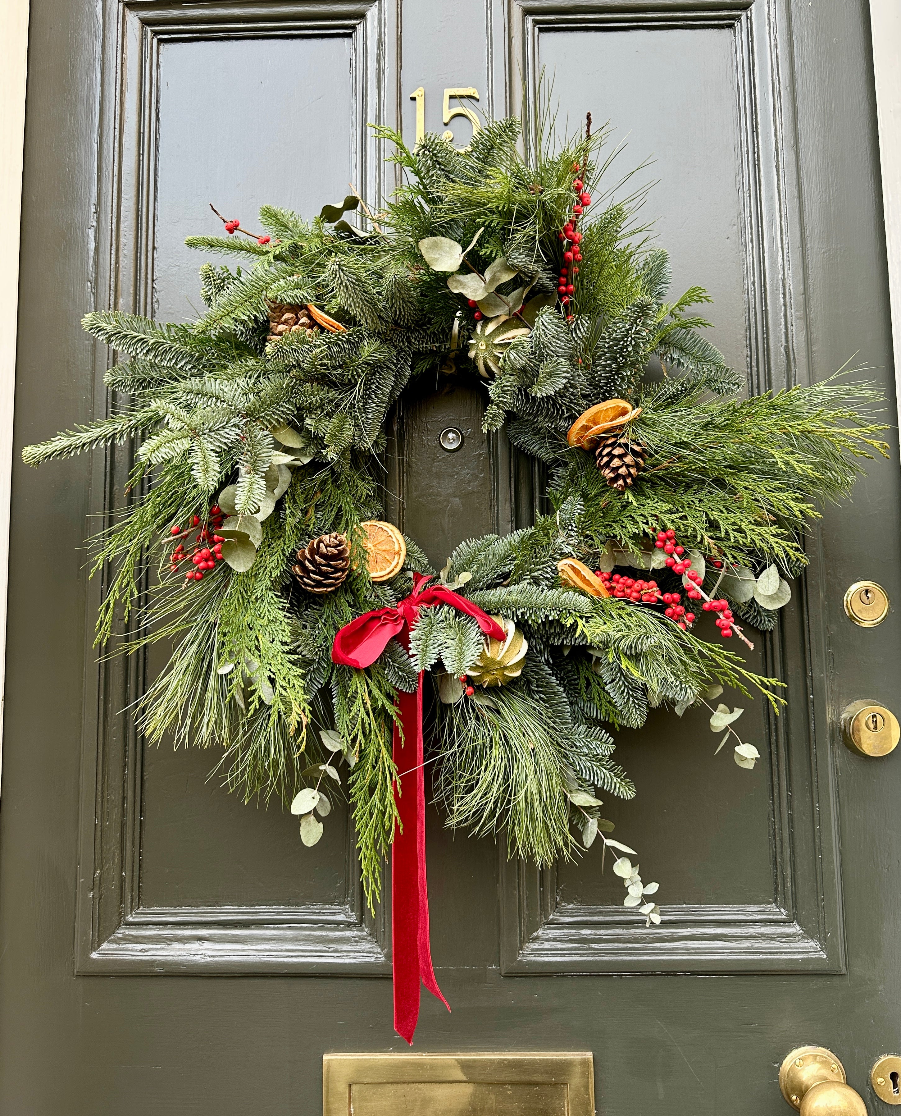 Christmas wreath with greenery, red ribbon, and decorations on a door.